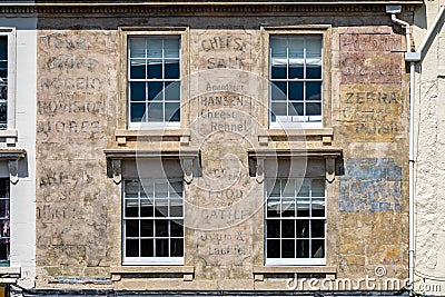 Vintage faded retail advertising signs from the early 1900`s painted on building wall at the top of Catherine Street, Frome, Somer Editorial Stock Photo