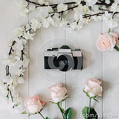 Vintage film camera in the middle, sakura branch, pink rose flowers on the white wooden desk. Top view, flat lay Stock Photo