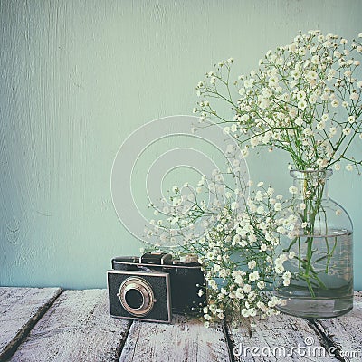 Vintage filtered and toned image of fresh white flowers and old camera over wooden table. Stock Photo