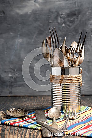 vintage forks, knives and spoons in a tin on a dark wooden table. Gray background, space for text Stock Photo