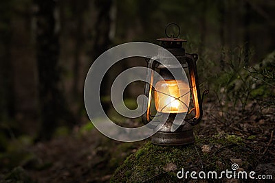 Vintage gasoline oil lantern lamp burning with a soft glow light in an dark forest / wood. Stock Photo