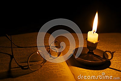 Vintage glasses on a bible lit by candlelight Stock Photo