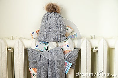 Vintage heating radiator with winter hat and scarf stuffed with euro money. The electricity bill goes up, European energy crisis. Stock Photo