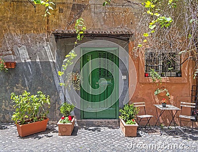 Vintage house exterior with green entrance door on ocher wall and flower pots. Stock Photo