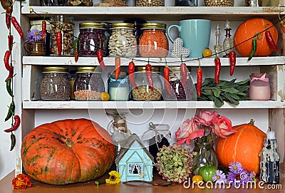 Vintage kitchen with wooden counters full of old utensils, bottles and jars with beans, herbs, spice, hanging hot pepper and Stock Photo