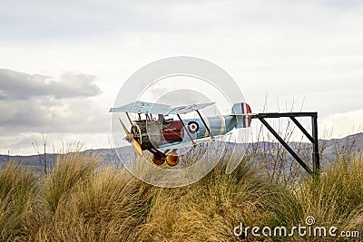 Vintage model airplane in blue, yellow, and red hues flying above tall grass, framed by majestic mountains Editorial Stock Photo