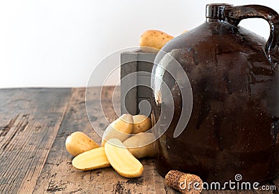 Vintage moonshine jug on a rustic wooden table with potatoes and corn cob cork Stock Photo