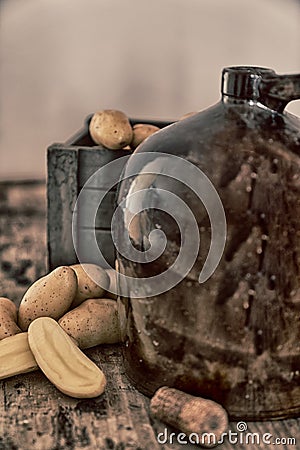 Vintage moonshine jug on a rustic wooden table with potatoes and corn cob cork Stock Photo