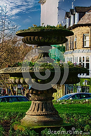 Vintage moss-covered fountain in a sunny park with blurred background of trees and buildings in Harrogate, England Stock Photo
