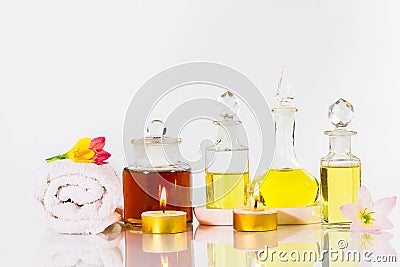 Vintage old bottles of aromatic oils with candles, flowers and white towel on glossy white table on white background Stock Photo