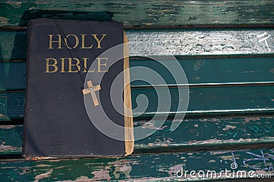 Vintage old holy bible book, grunge textured cover with wooden christian cross. Retro styled image on wood background. Stock Photo