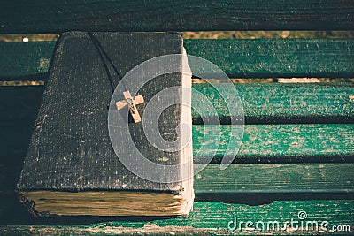 Vintage old holy bible book, grunge textured cover with wooden christian cross. Retro styled image on wood background. Stock Photo