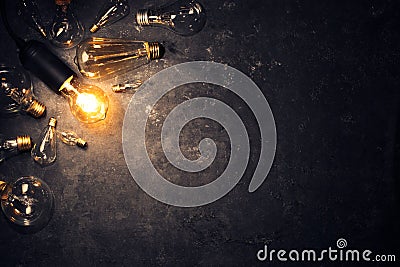 Vintage old light bulb glowing on rough dark background surrounded by burnt out bulbs. Idea, creativity concept Stock Photo