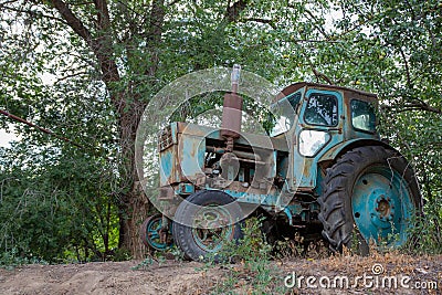 Vintage photo - an old blue tractor standing under a green branching tree Stock Photo