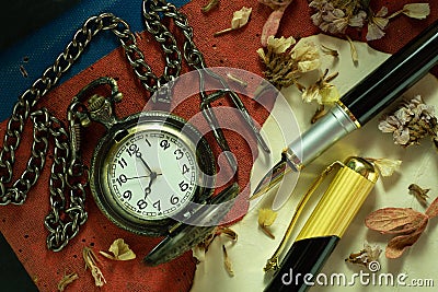 Vintage pocket watch and brass pen on old book. Stock Photo