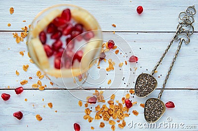 Vintage spoons with chia, scattered granola grains and pomegranate seeds on the white wooden table. Granola pudding Stock Photo