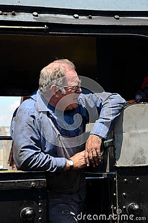 Vintage steam train driver in coal soiled blue overalls in locomotive cab Editorial Stock Photo