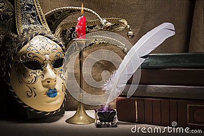 Vintage still life with old books near inkstand, feather, venezian mask and burning red candle in candlestick on canvas background Stock Photo