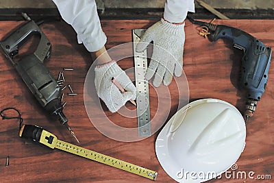 Vintage toned image. Aerial view of hands of carpenter working on wooden board with tools background. Measuring tape , safety hel Stock Photo