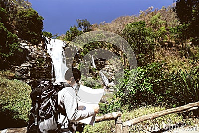 Vintage toned image of young backpacker exploring map on his hands in waterfall national park background. Stock Photo