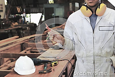 Vintage toned image of young carpenter in white safety uniform holding a pencil in hands in wood workshop background. Industrial c Stock Photo