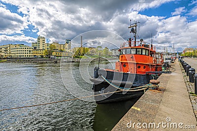 Vintage tugboat moored at Hammarby canal embankment in front of Lumafabriken works The Luma bulb Factory at sunny spring day. Editorial Stock Photo