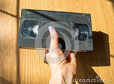 Vintage videotape in a woman& x27;s hand on a wooden table., on beige background. Stock Photo