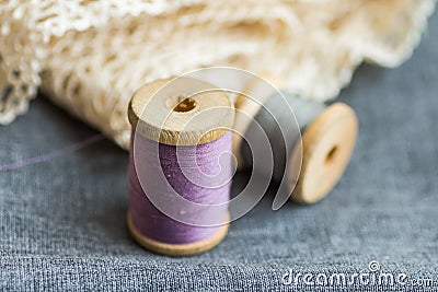 Vintage wood spools with lilac and grey threads on folded wool fabric, cotton off-white lace, hobby swing concept Stock Photo