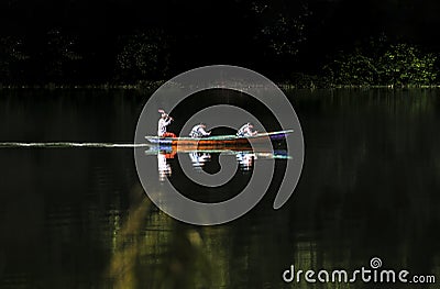 Traditional wooden boat passes silently in the tranquil lake environment Editorial Stock Photo