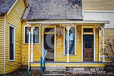 Vintage yellow frame duplex with wood shingle roof and porch with old ornate pillars - grungy Stock Photo