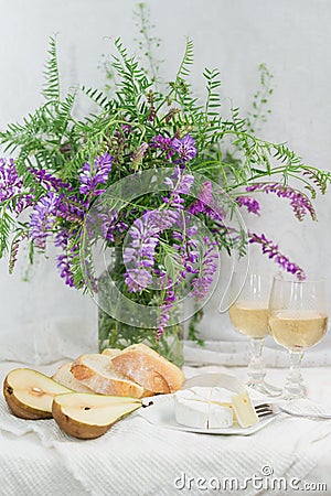 Violet flowers, pears, brie cheese and wine glasses. Still life Stock Photo