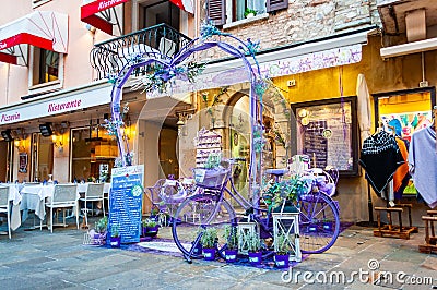 Violet purple vibrant heart shape arc, bicycle and bench decoration at the entrance to the lavender shop in the center of Sirmione Editorial Stock Photo