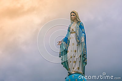 Virgin Mary statue at Catholic church with sunlight in cloudy day background. Stock Photo