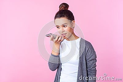 Virtual assistant. Portrait of teenage brunette girl talking to phone using digital voice app. studio shot isolated on pink Stock Photo