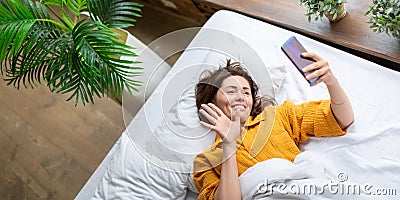 Virtual love - woman lies in bed with cell phone. Online call to virtual boyfriend. Format photo 2x1. Stock Photo