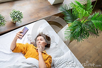 Virtual love - woman lies in bed with cell phone. Online call to virtual boyfriend. View from the top. Stock Photo