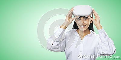 Virtual reality concept: smiled young woman in light shirt with VR glasses on her head on light green background with place for Stock Photo