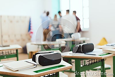 Virtual reality headsets on tables with teacher and high school students standing behind Stock Photo