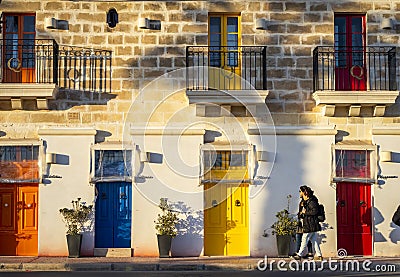 Visitors walk in front of the building with colorful doors at Malta Marsaxlokk Editorial Stock Photo