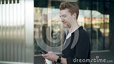 Vista lateral del hombre joven sonriente con smartphone y del café que escuchan la música almacen de video Vista lateral del hombre joven sonriente con smartphone y del café que escuchan la música almacen de video