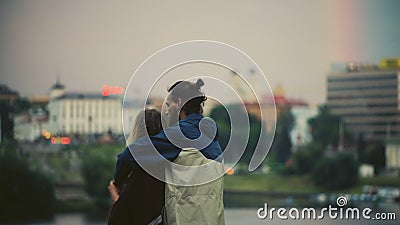 Vista trasera de los pares felices que miran en el panorama de la ciudad en puesta del sol El hombre abraza la mujer y el goce de metrajes Vista trasera de los pares felices que miran en el panorama de la ciudad en puesta del sol El hombre abraza la mujer y el goce de metrajes