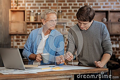 Pleasant mentor helping young colleague draw blueprint Stock Photo