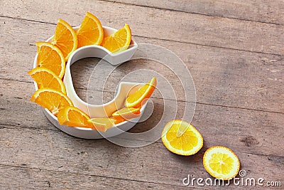 Vitamin C or ascorbic acid nutrient in food concept. Plate in shape of letter C with orange slices on wooden background. Flatlay Stock Photo