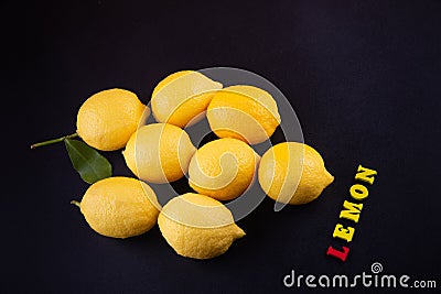 Vitamin C. Several fresh yellow lemons laying on black table near small wooden letters Stock Photo