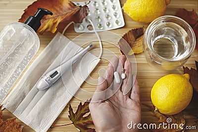 Vitamin D, C and zinc pills in hand on background of fall leaves, face mask, sanitizer, lemons Stock Photo