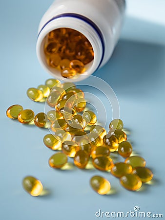 Bottle with vitamins capsules on a blue surface. Omega and vitamin D. Nutritional supplements. Opened bottle with yellow pills Stock Photo