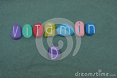 Vitamin D text composed with multi colored stone letters over green sand Stock Photo