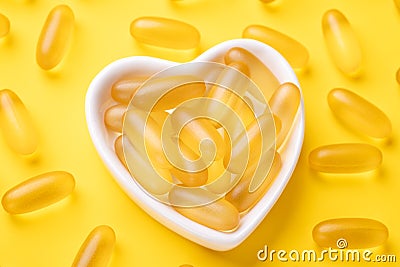 Vitamin D and Omega 3 fish oil capsules supplement in a heart-shaped plate on yellow background. Concept of healthcare Stock Photo