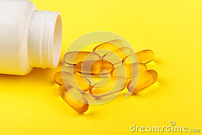 Vitamin D yellow pills on yellow background and white plastic jar. Medicine gel tablets of vitamin d on table. Yellow Stock Photo