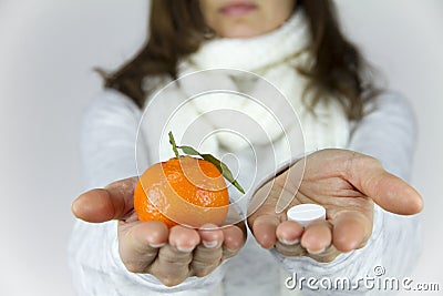 Vitamins from fruit or drugs? A sick young woman with a scarf on her neck shows a mandarin in her right hand and an aspirin on her Stock Photo